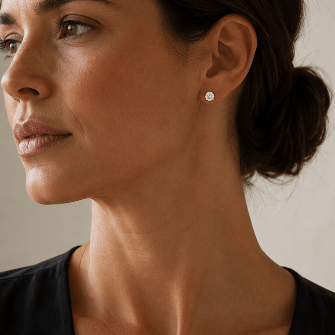 Woman wearing a 1-carat moissanite diamond stud earring and black sleeveless top with a neutral background