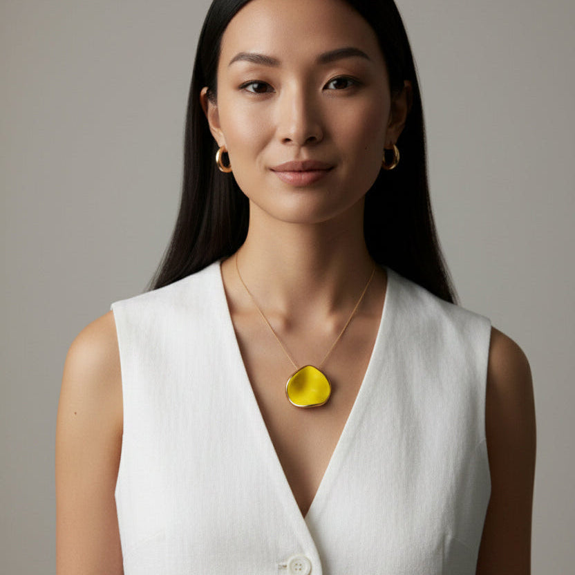 Woman wearing a white shirt with a yellow flower pendant necklace against a neutral background