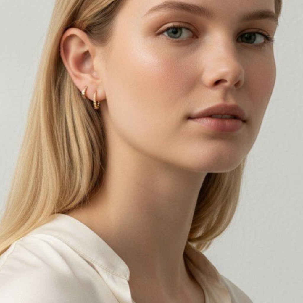 IRLÔH gold plated sterling silver huggie hoop earrings with cubic zirconia stones, worn by a blonde model.