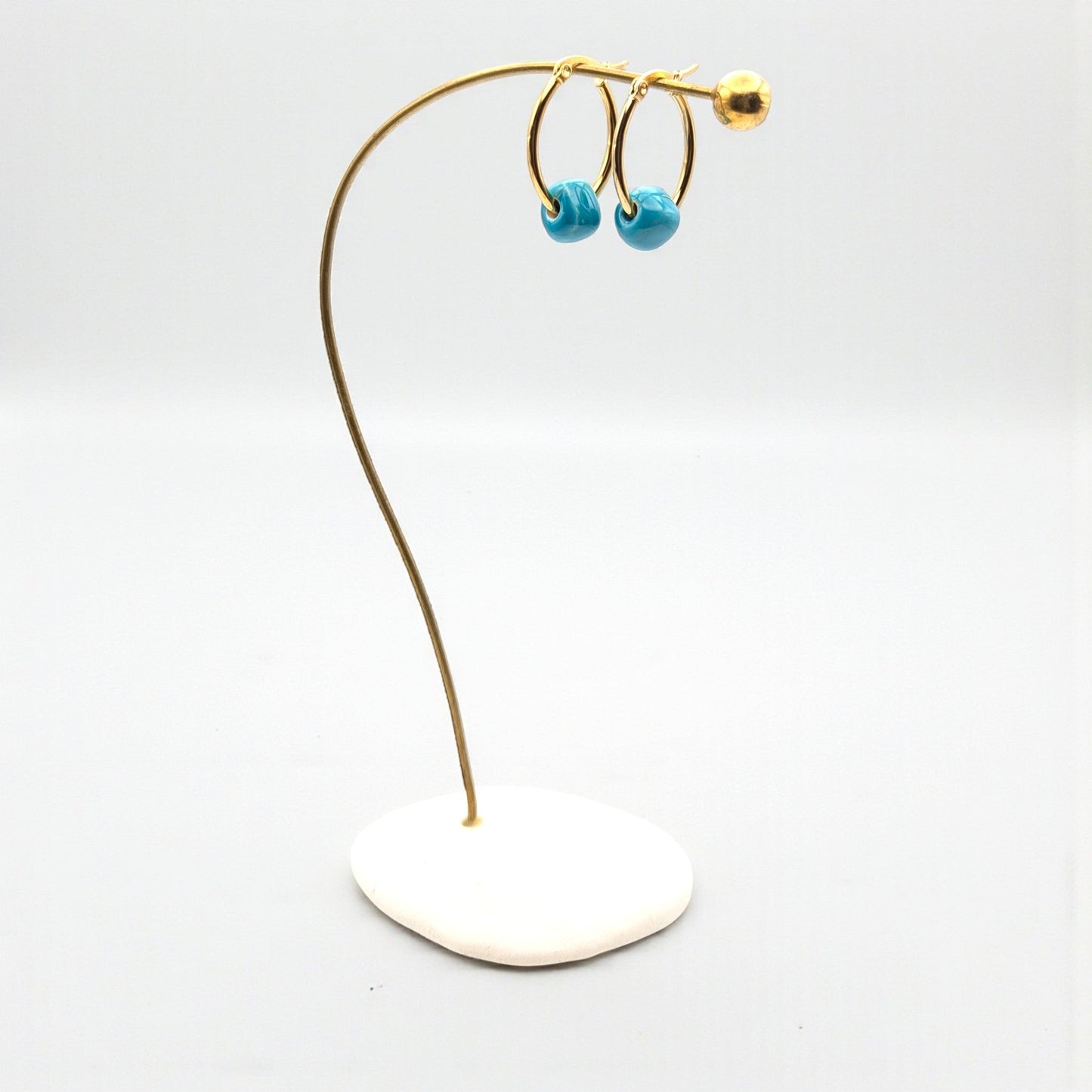 Maximilianas gold oval hoop earrings with removable turquoise bead on product stand