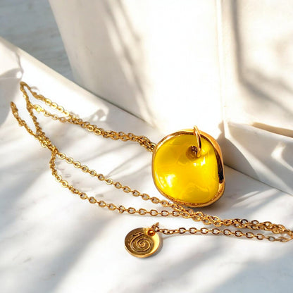 Maximilianas yellow ceramic pendant necklace with a gold chain, displayed on a white fabric surface.