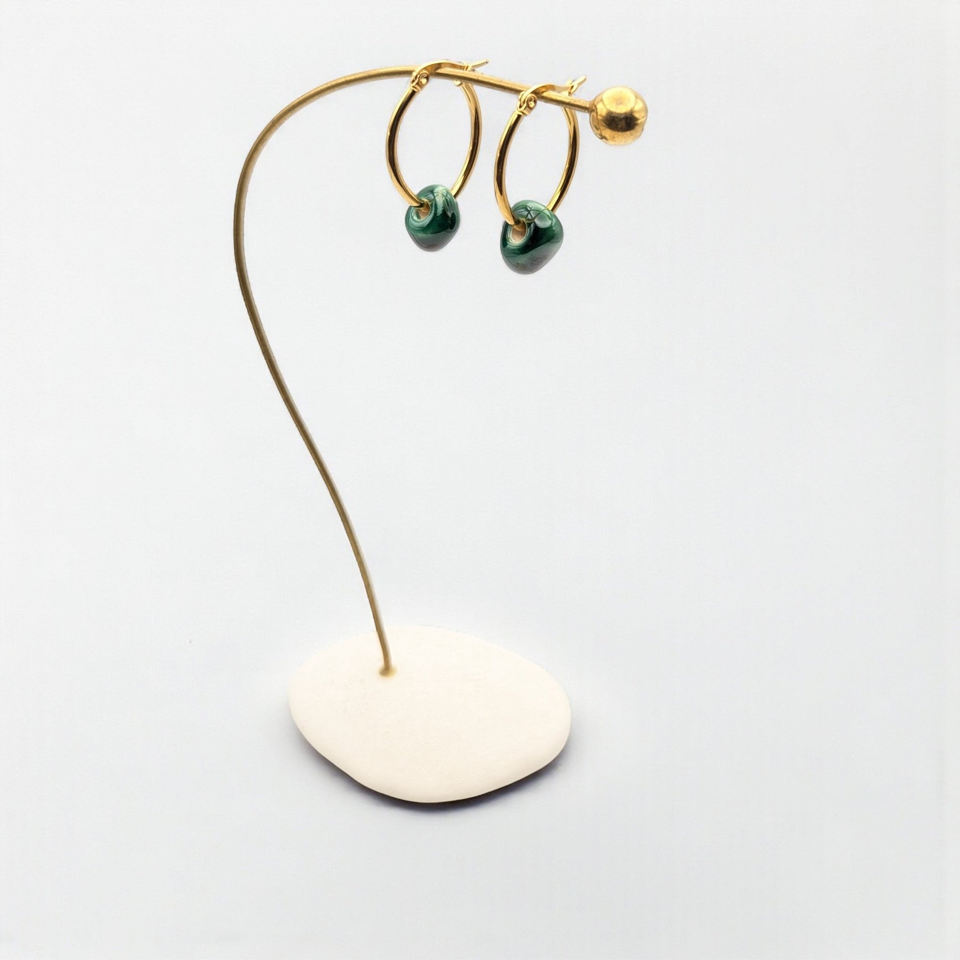 Maximilianas Petra oval hoop earrings in 18K gold plated stainless steel and green ceramic bead on a stand