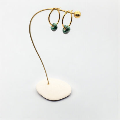Maximilianas Petra oval hoop earrings in 18K gold plated stainless steel and green ceramic bead on a stand