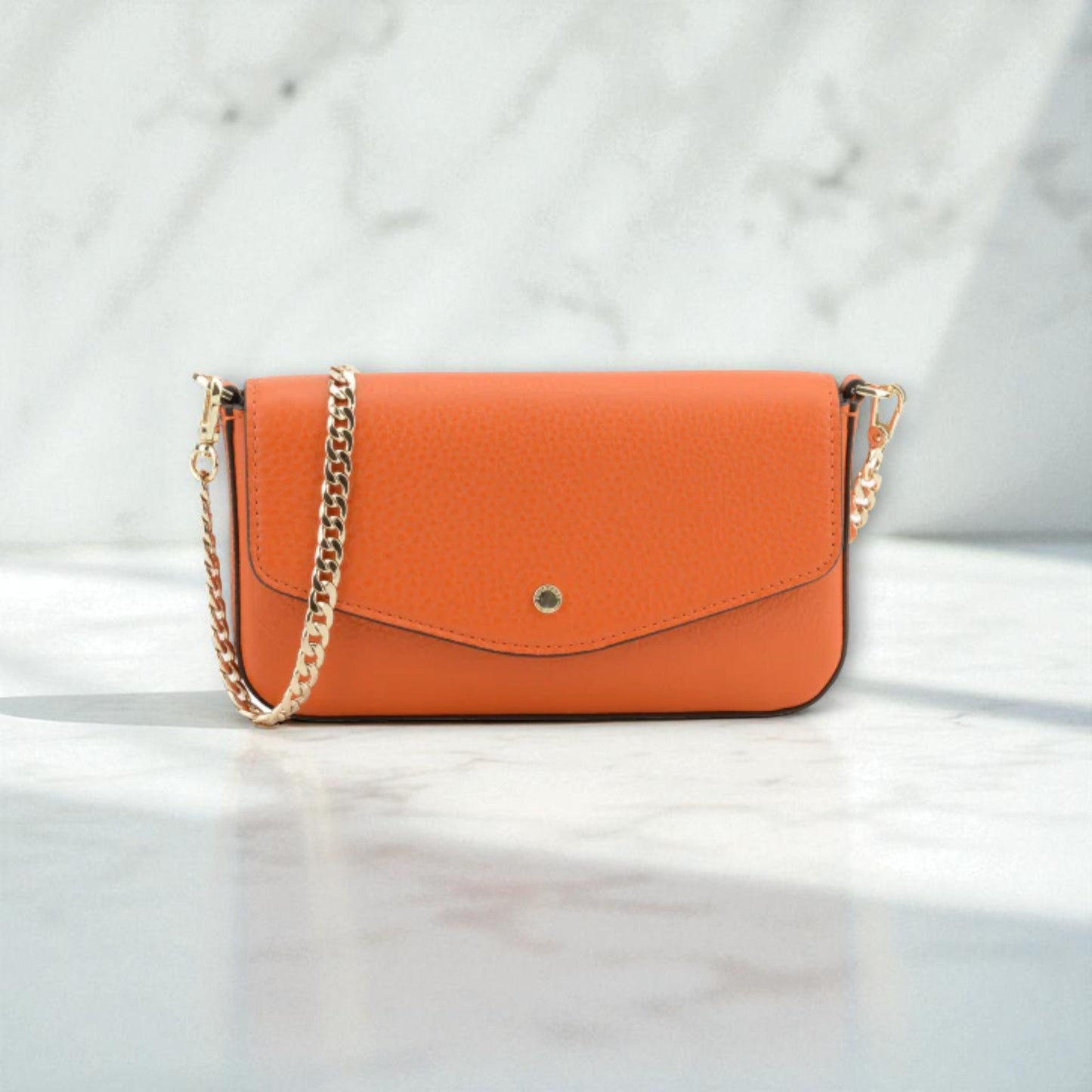 Front view of Pourchet Club orange clutch bag with a gold chain on a light marble background.