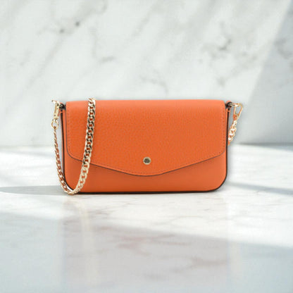 Front view of Pourchet Club orange clutch bag with a gold chain on a light marble background.