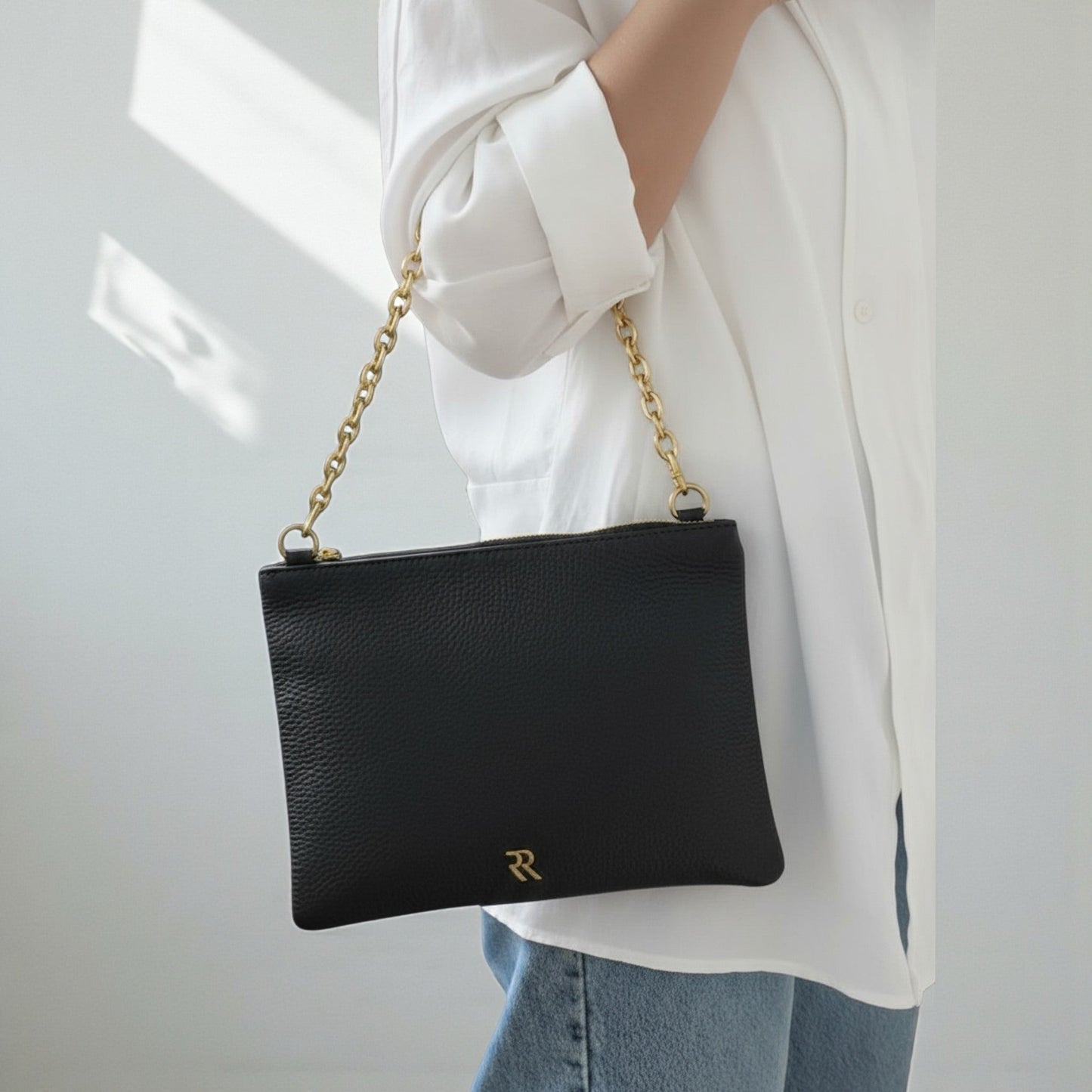 Rossi black leather pouch with chain strap held by a person wearing a white shirt and blue jeans.