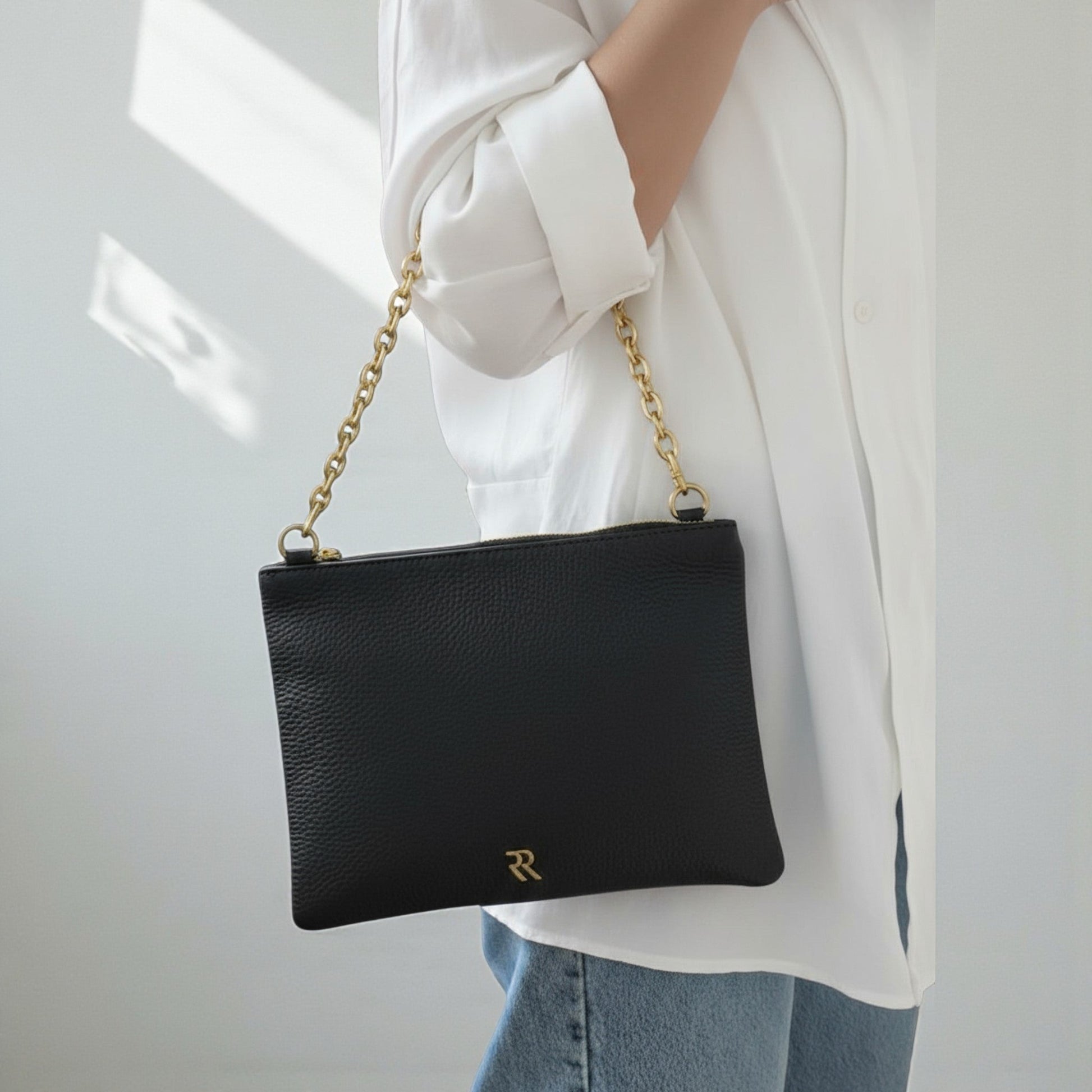 Rossi black leather pouch with chain strap held by a person wearing a white shirt and blue jeans.